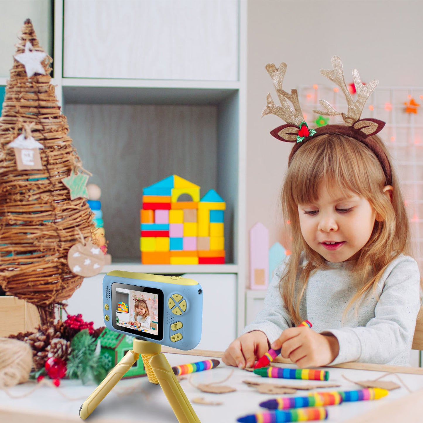 Child with reindeer headband using a toy camera, surrounded by Christmas decorations.